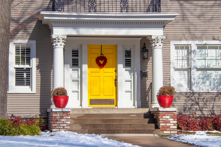 An exterior view of a house with a bright yellow entry door and white single-hung windows An exterior view of a house with a bright yellow entry door and white single-hung windows