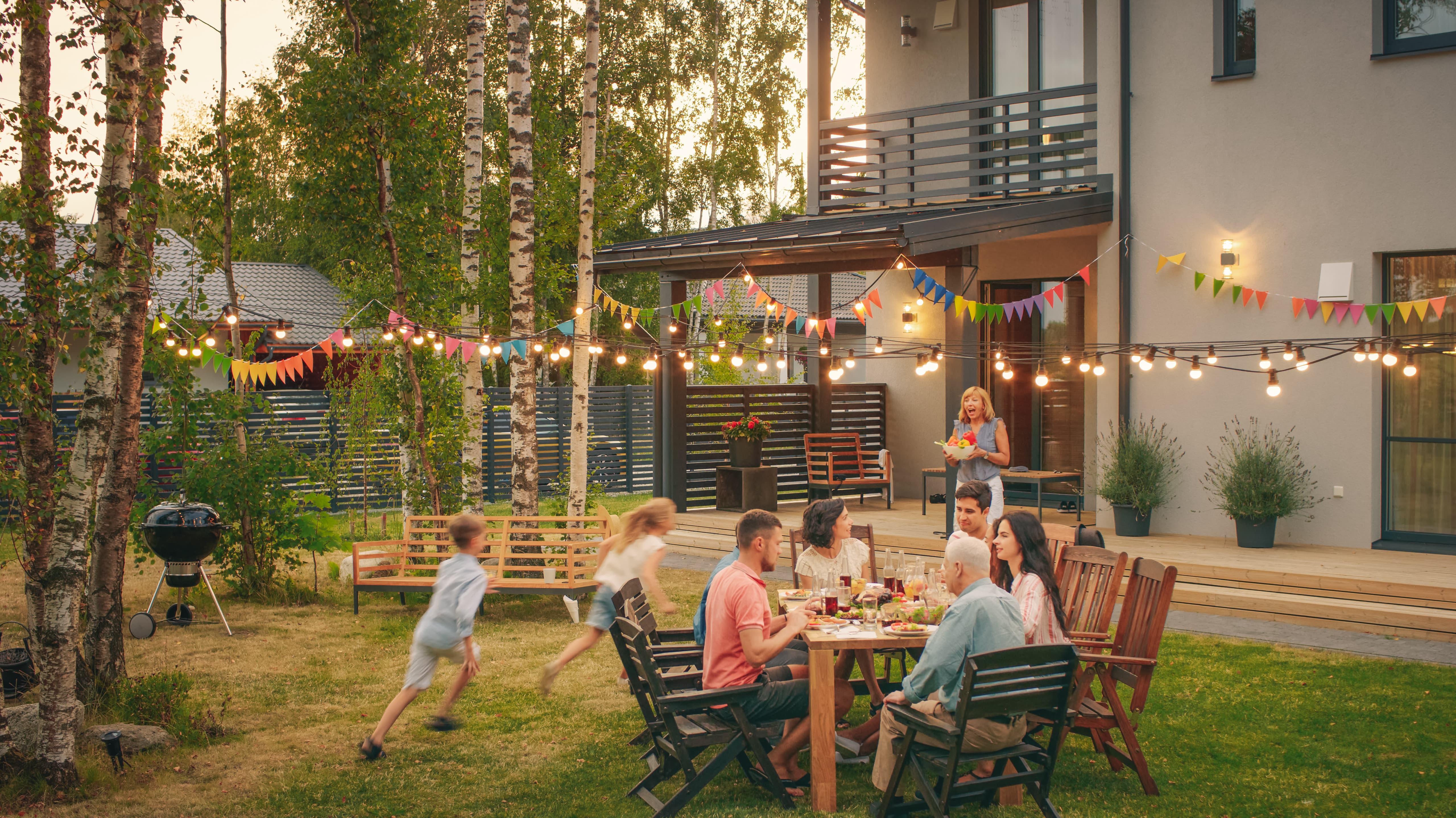 Children playing in backyard as parents sit at a table conversing Children playing in backyard as parents sit at a table conversing