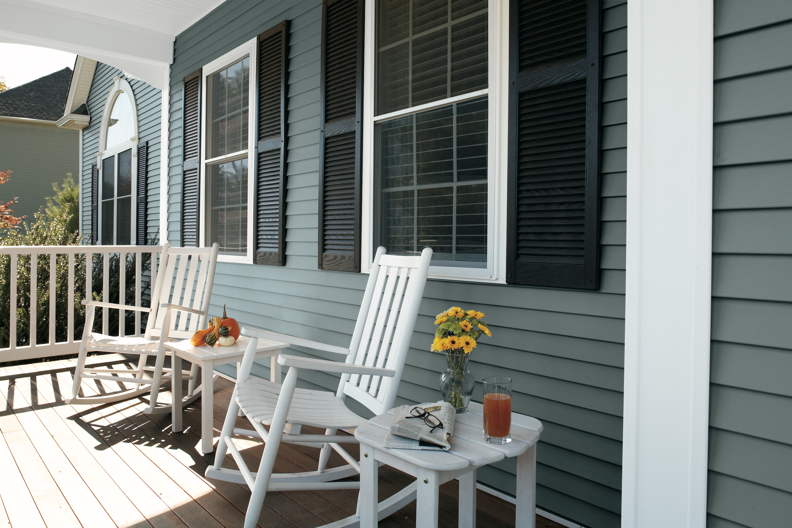 Porch of a home with blue vinyl siding and two white rocking chair