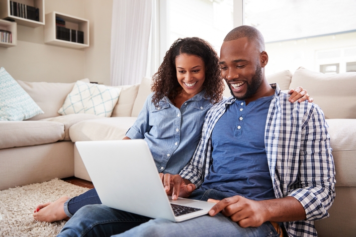 Happy couple looking at laptop in living room Happy couple looking at laptop in living room