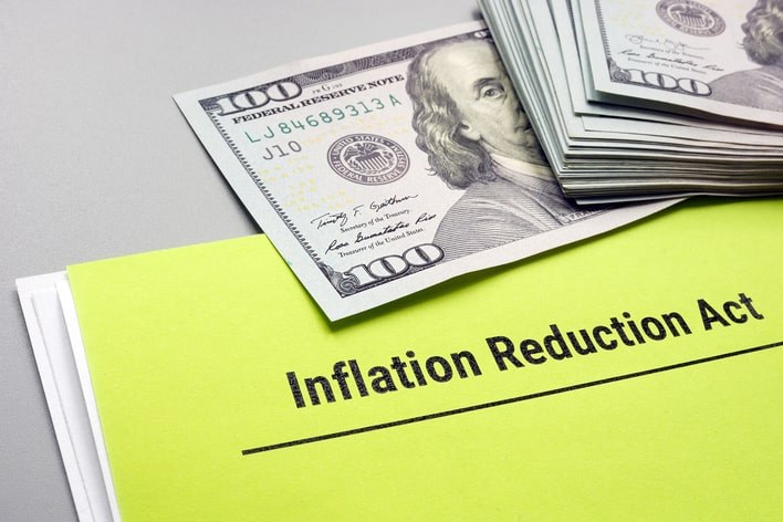 Stack of 100 dollar bills on top of paper that reads "Inflation Reduction Act"
