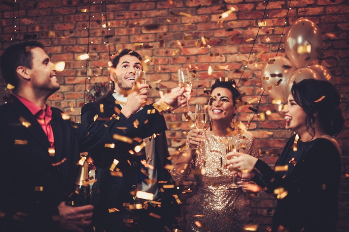 Gold confetti falling on 2 men and 2 women at a New Year’s Eve party